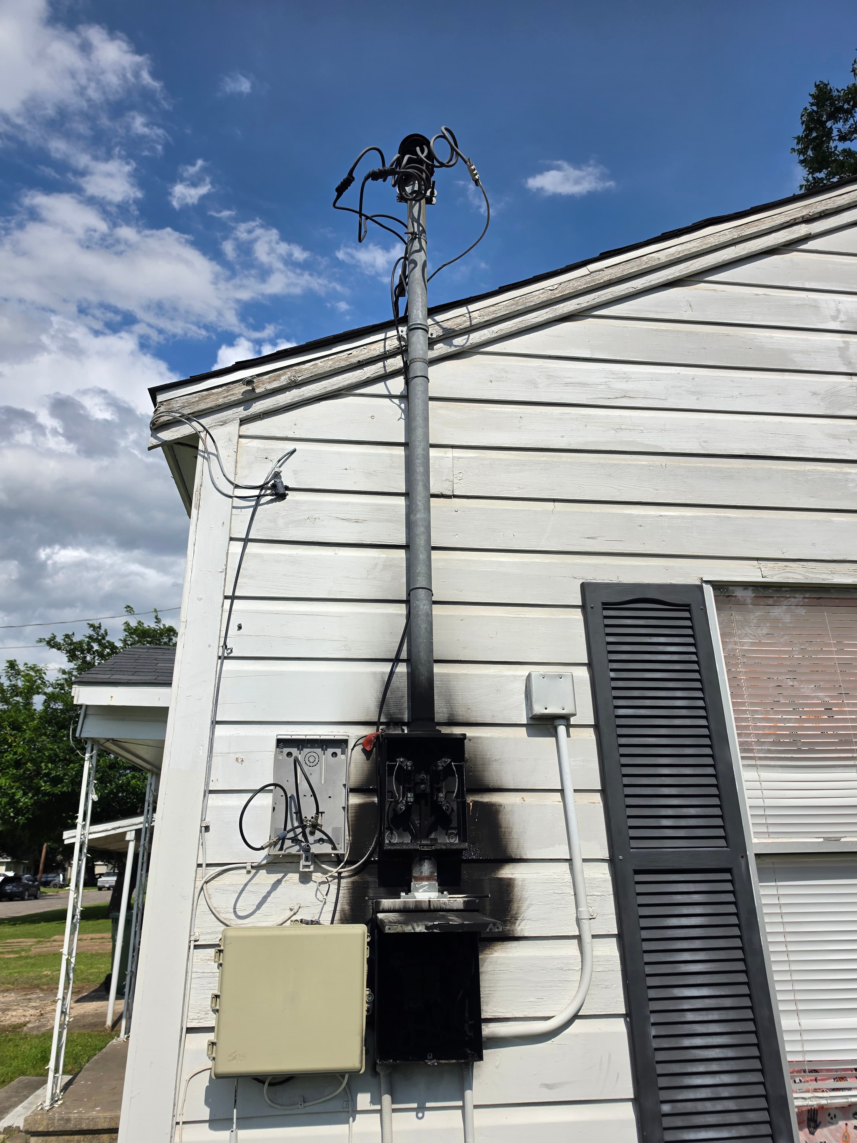 Fire-damaged electrical meter box with black charring on the white siding of a house.
