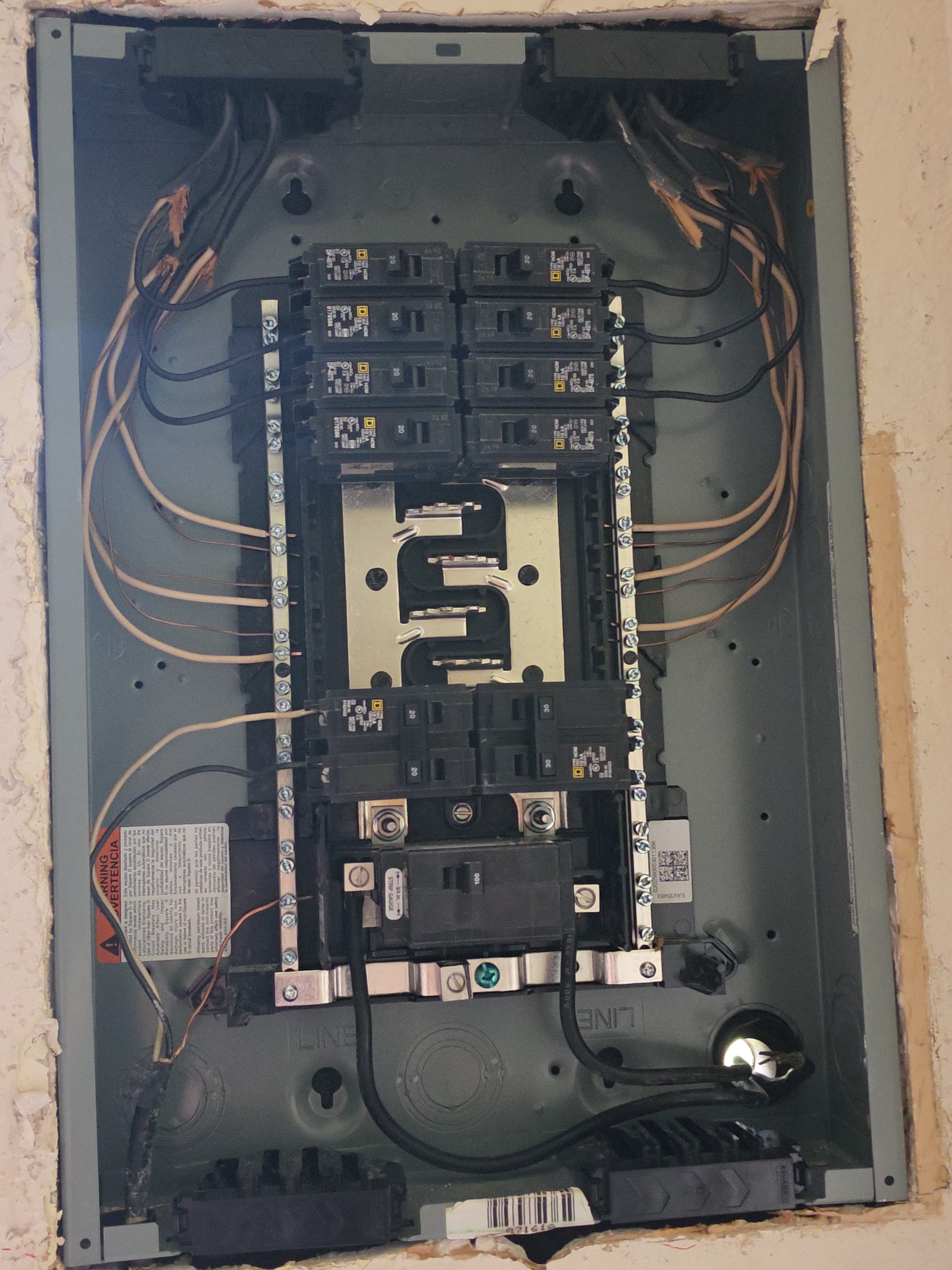 Open electrical service panel with multiple circuit breakers and wiring connected to bus bars.
