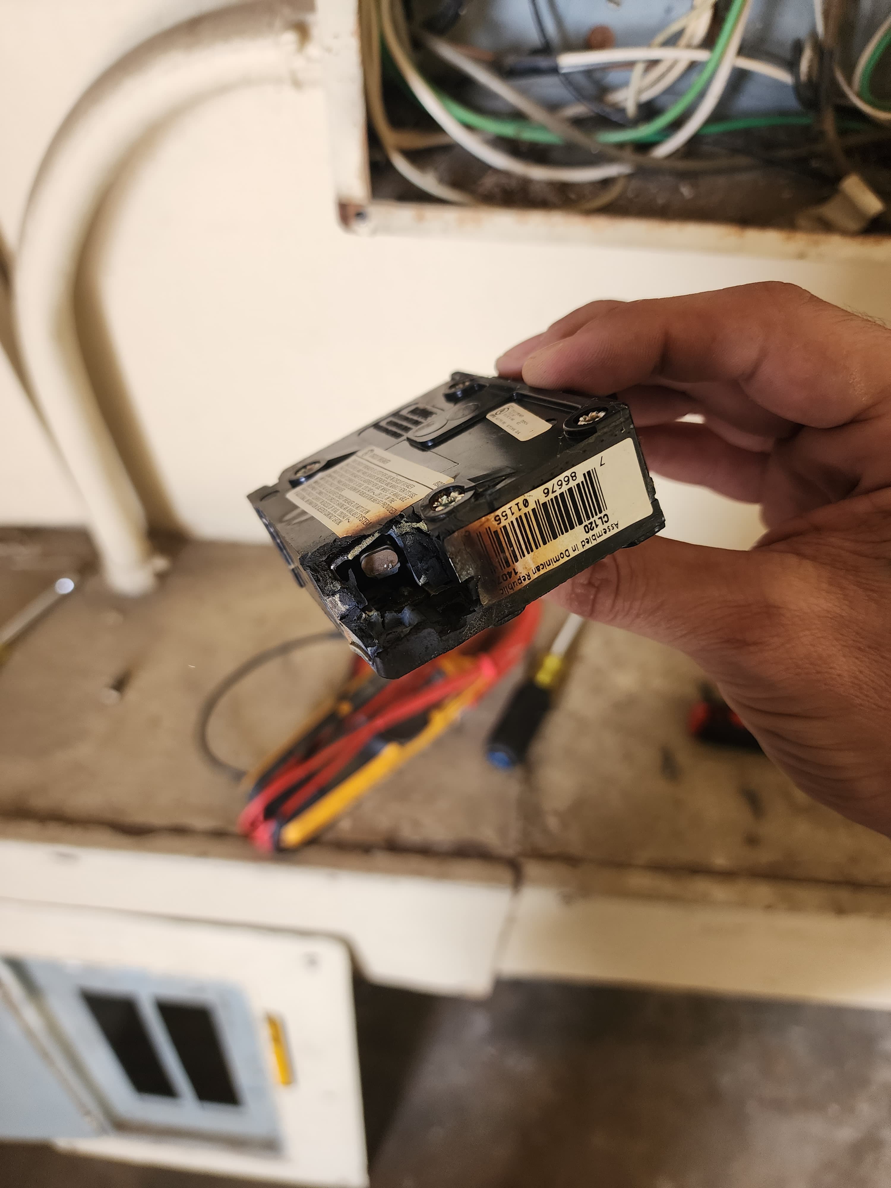Hand holding a black circuit breaker with severe melting and charring around its terminal.