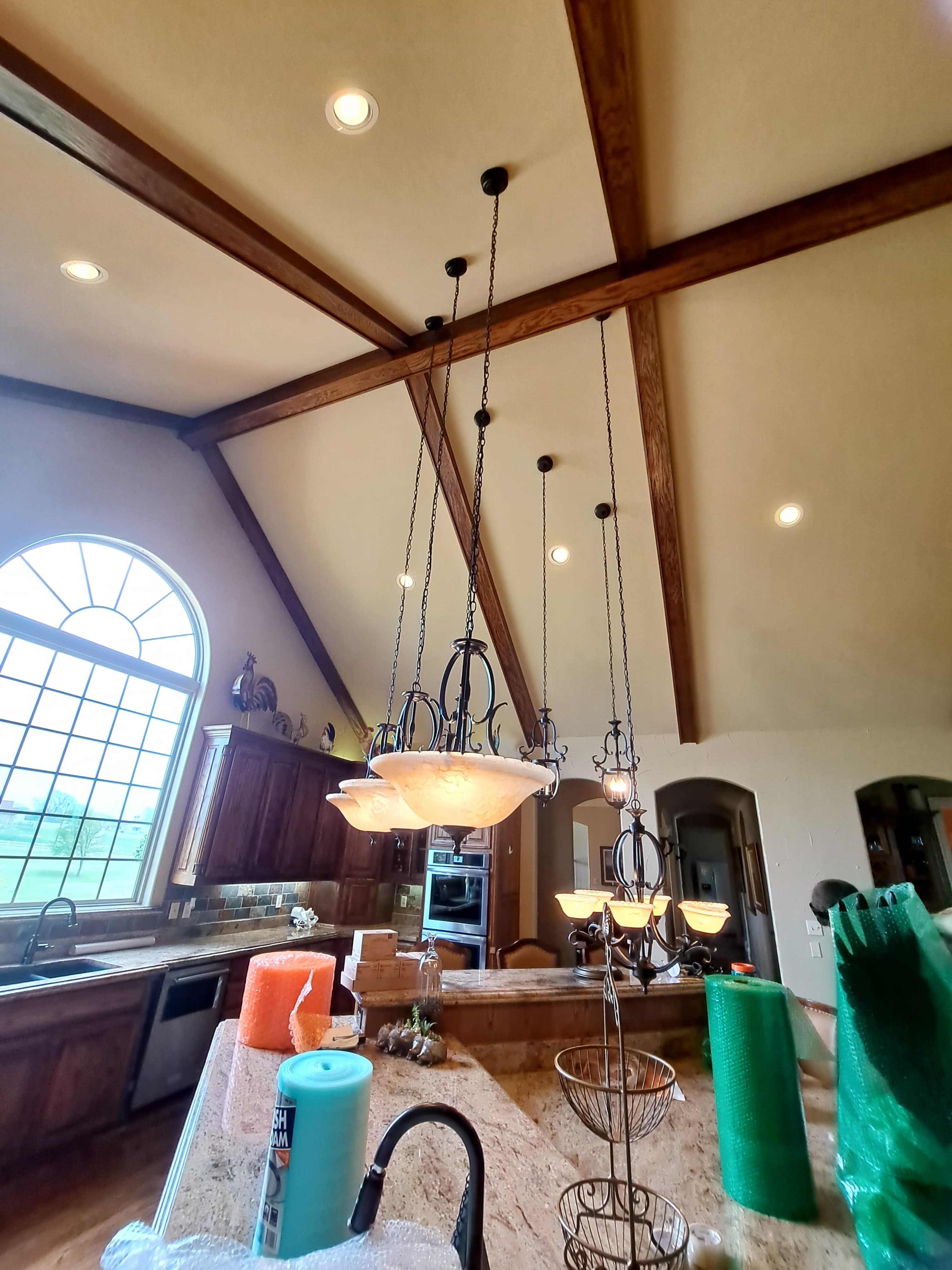 Kitchen with vaulted wood-beamed ceilings, a large arched window, and multiple hanging light fixtures.