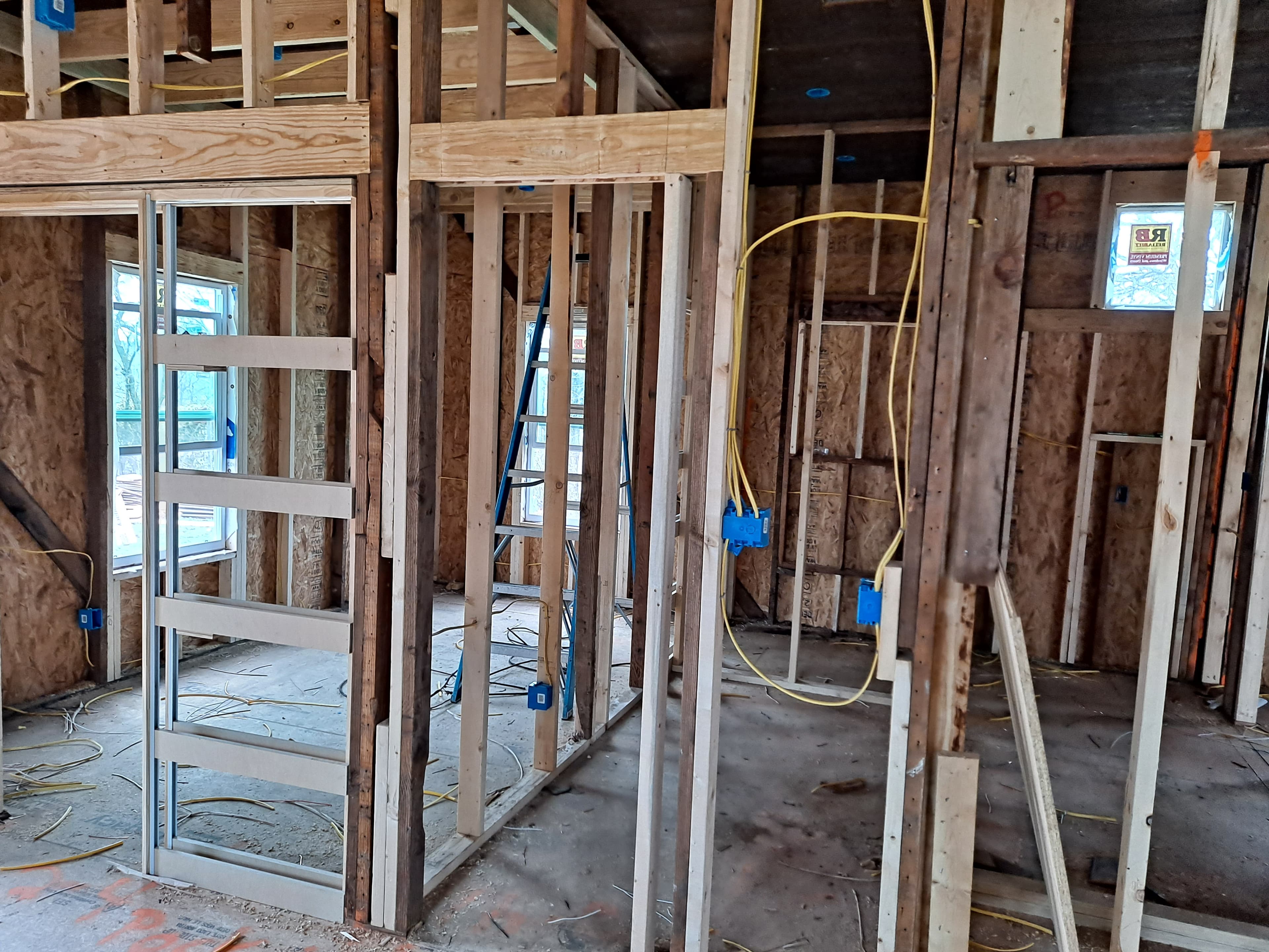 Interior house framing featuring wooden studs, yellow electrical wiring, and blue junction boxes under construction.