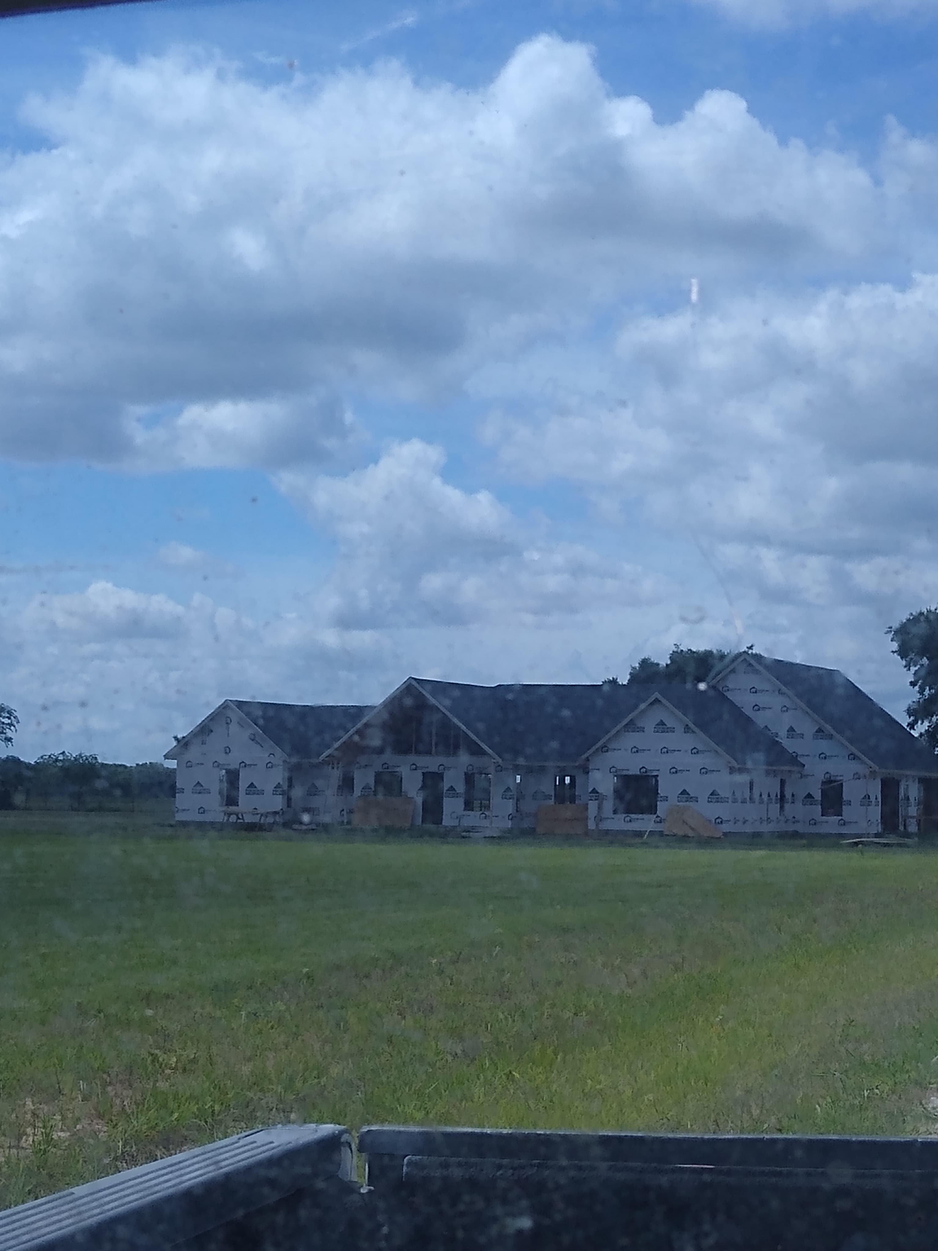 Large house under construction with white house wrap in a grassy field under cloudy skies.