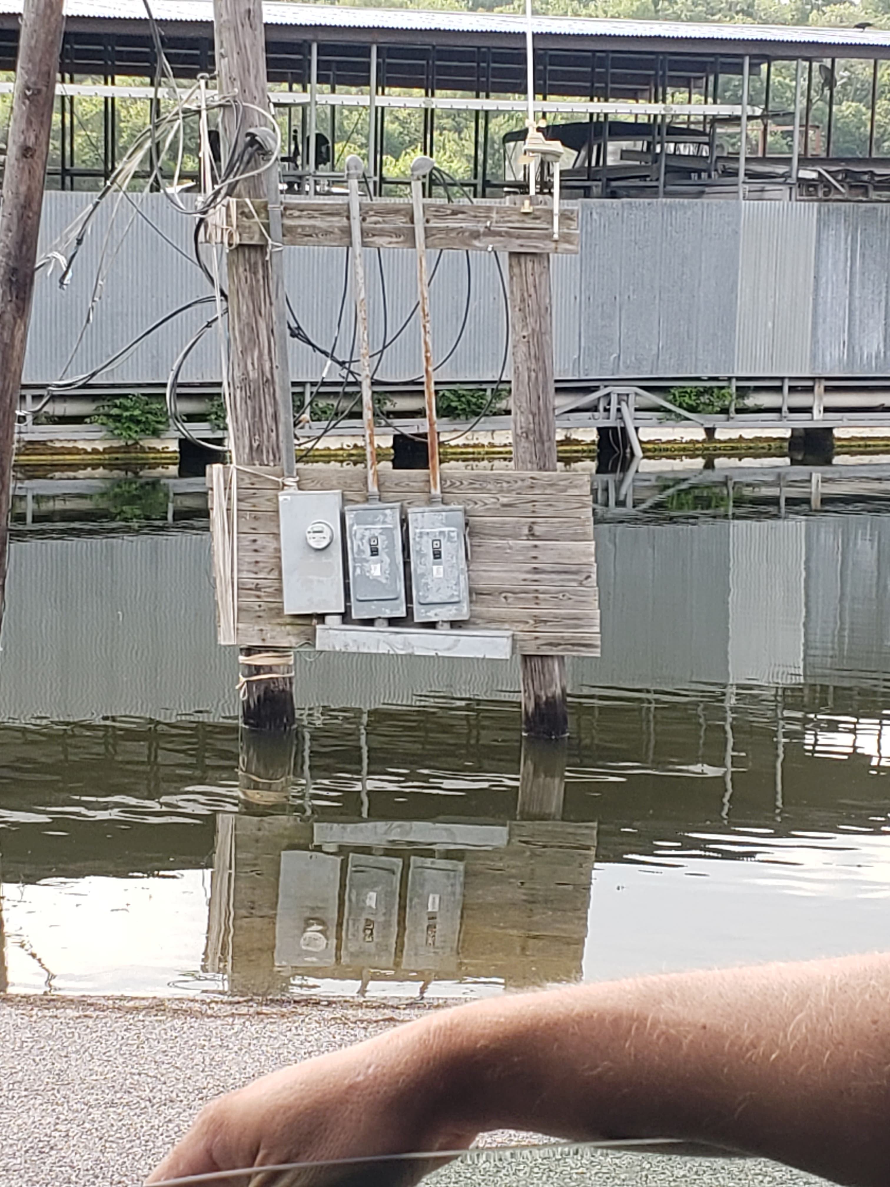 Three electrical panels mounted on wooden posts over water, reflecting clearly on the surface.