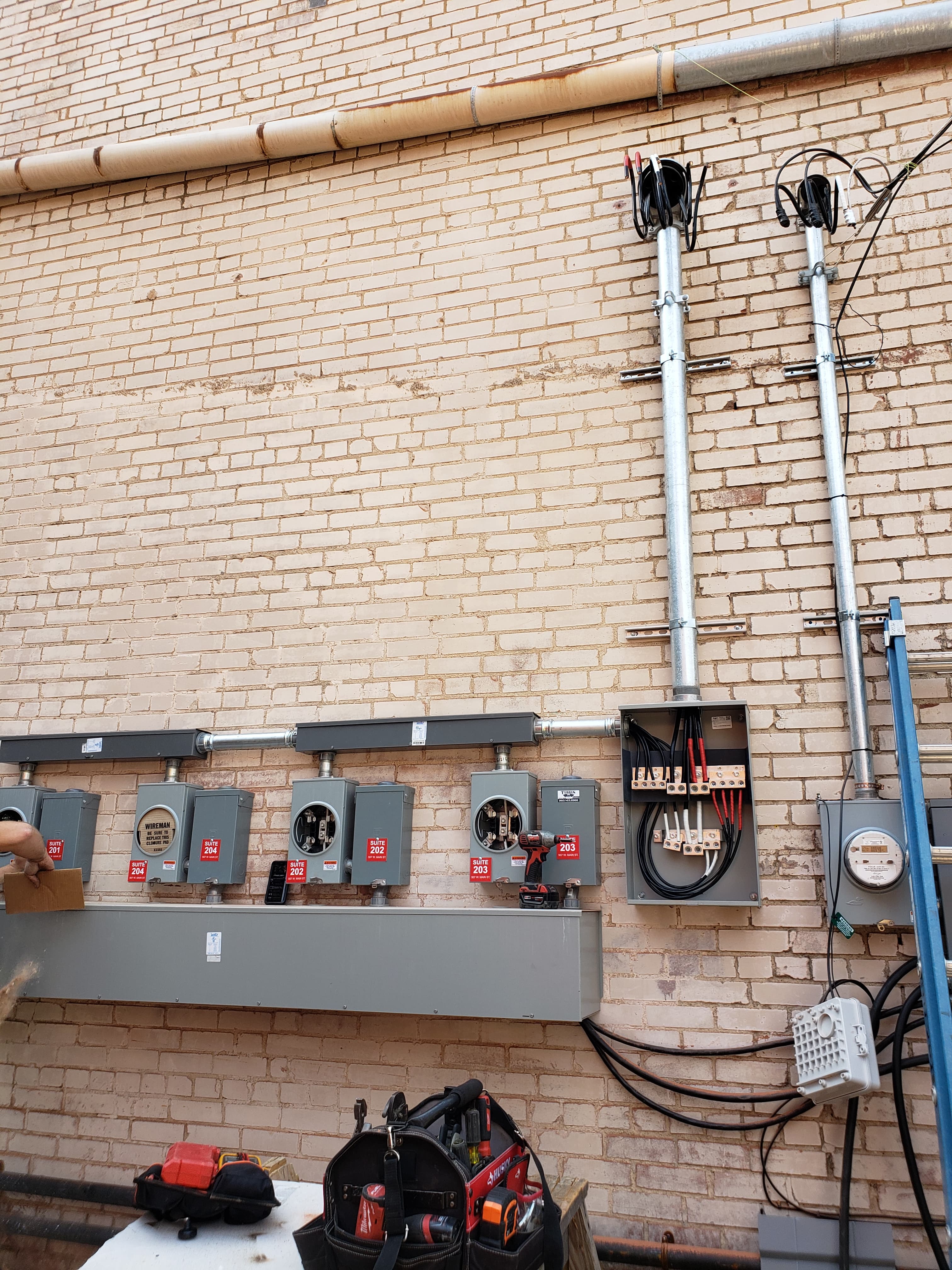Electrical meter sockets and panels labeled with suite numbers on a brick wall with conduits.